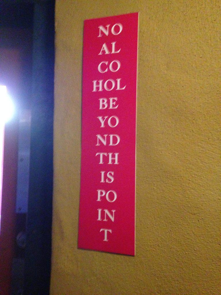 Een heel smal bord met de tekst "geen alcohol voorbij dit punt". Er zijn gemiddeld 2 letters op elke regel. De tekst is vrijwel onleesbaar en ziet eruit als een lijst met afkortingen.